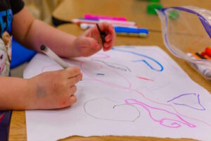 Photo of a preschooler drawing on a paper sheet.